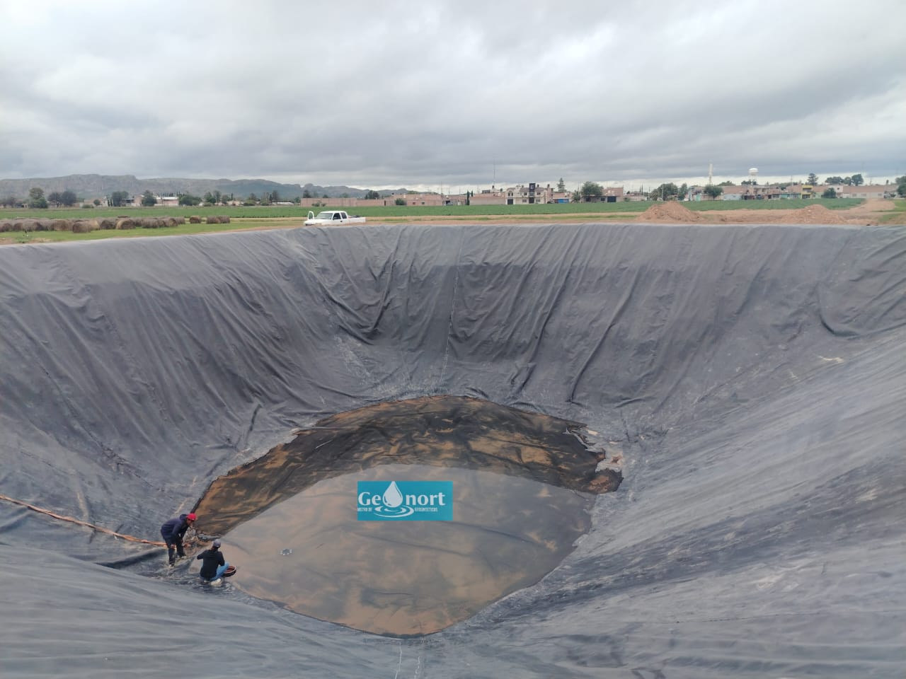 Vista elevada de una superficie recubierta con geomembrana, con personas en la parte inferior